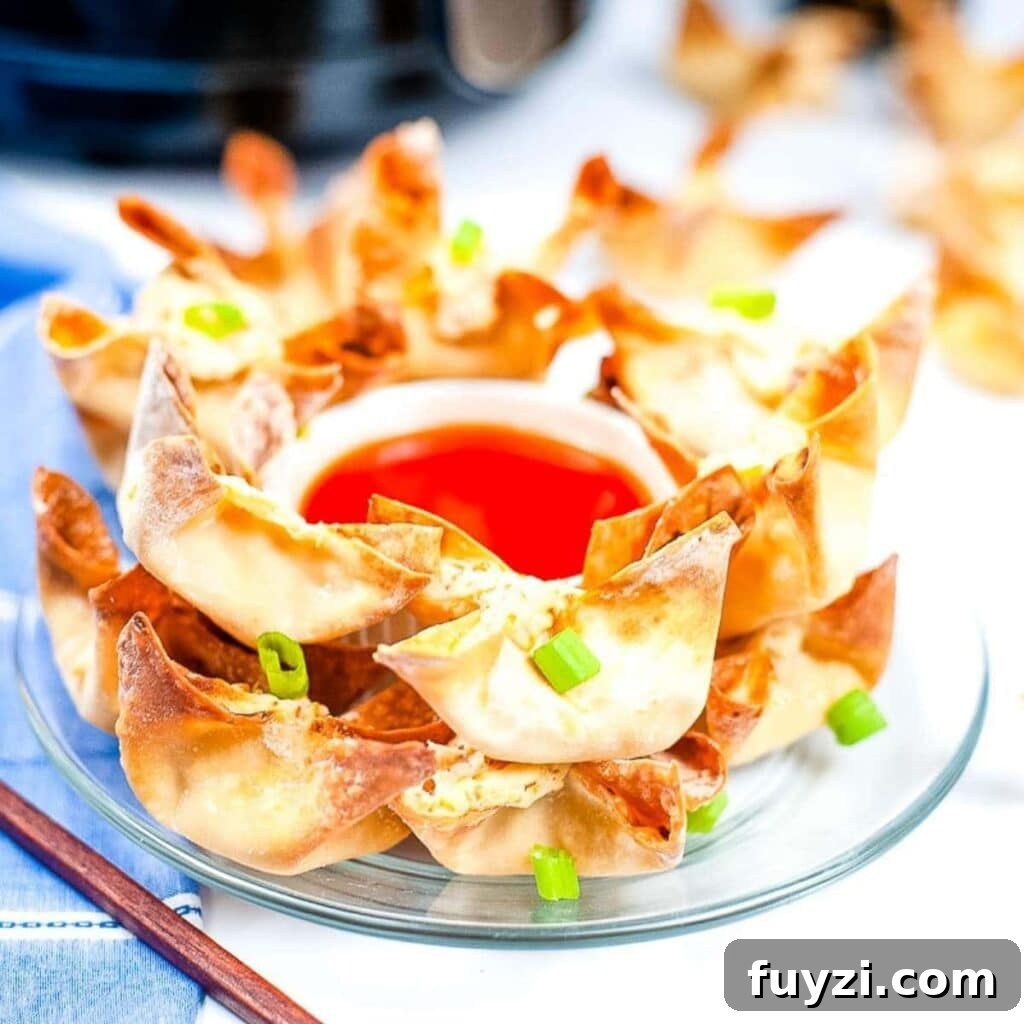 Crispy Air Fryer Crab Rangoon Recipe 2 Air fried crab rangoon stacked on a glass plate with a bowl of sweet and sour dipping sauce.