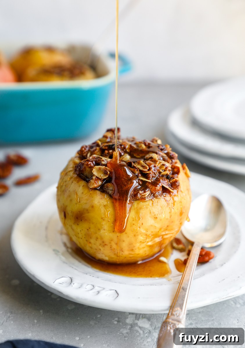 A baked apple stuffed with oat crumble and drizzled with honey sauce sitting on a white plate with a spoon