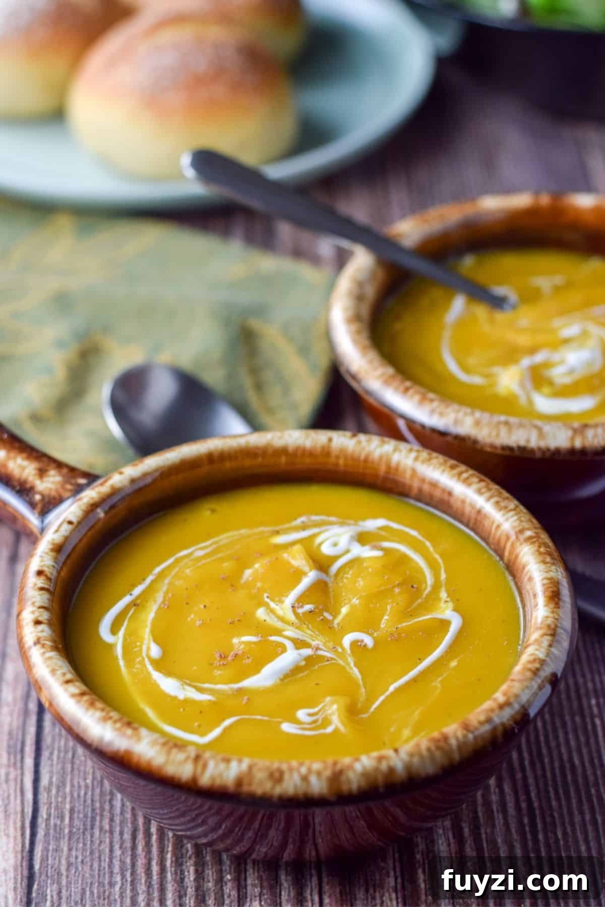 Creamy Roasted Butternut Squash Soup Recipe 7 close view of two brown crocks filled with squash soup with sour cream squiggled on top