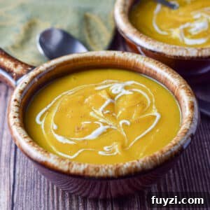 Two brown crocks filled with squash soup with sour cream squiggled on top - square