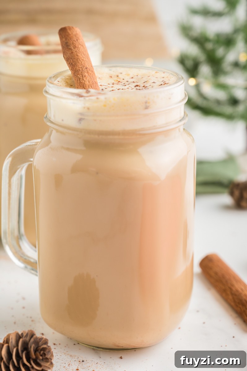Eggnog Latte in a clear mug with cinnamon sticks and a Christmas tree and pine cone on the side.