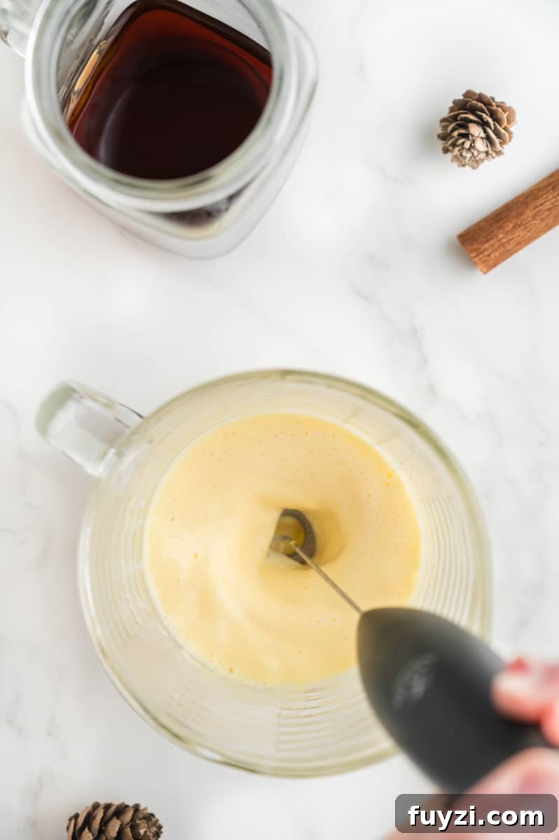 A handheld frother whipping eggnog into foam.