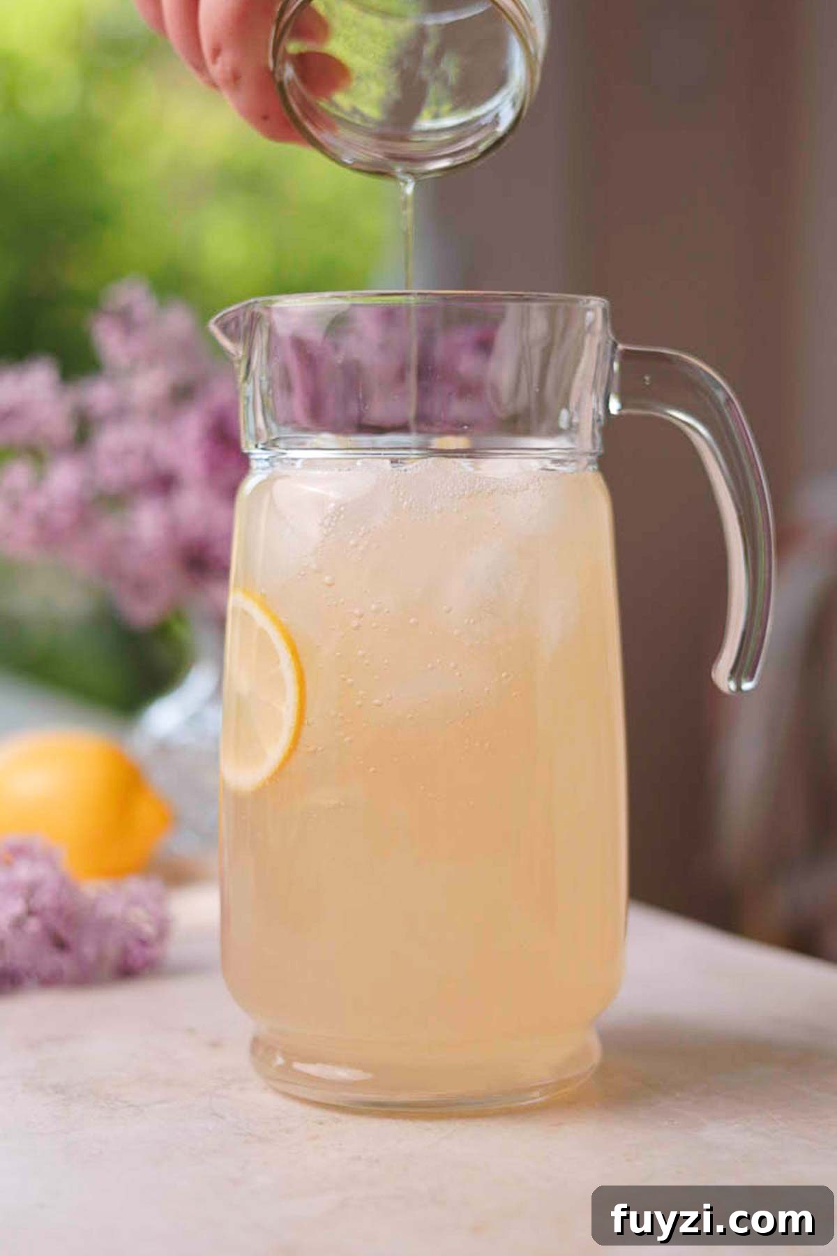 Lilac Lemonade Recipe: How to Make a Floral Citrus Drink 11 pouring lilac syrup into a pitcher full of lemon juice, water, and ice