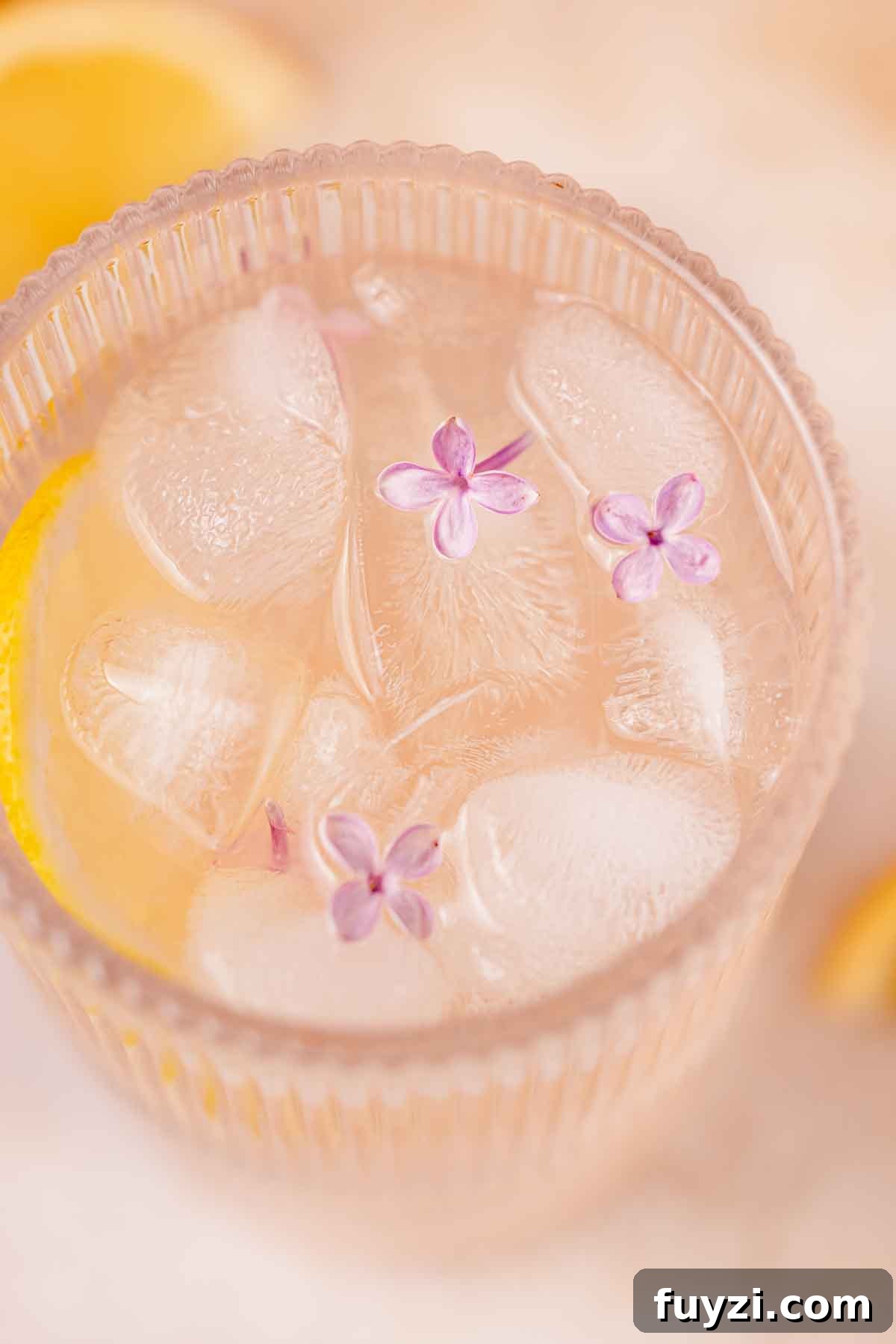 Lilac Lemonade Recipe: How to Make a Floral Citrus Drink 14 closeup of lilac lemonade in a glass with ice cubes and three lilac blossoms