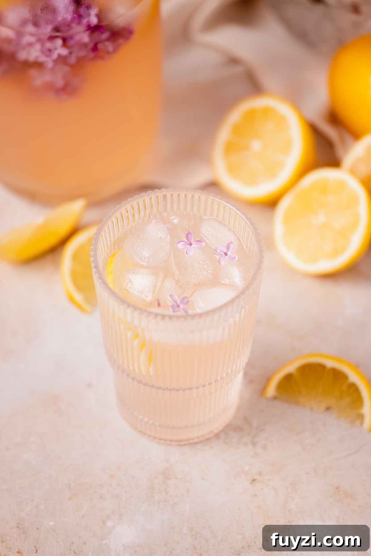 Lilac Lemonade Recipe: How to Make a Floral Citrus Drink 3 lilac lemonade in large glass with three small lilac blossoms on top of ice