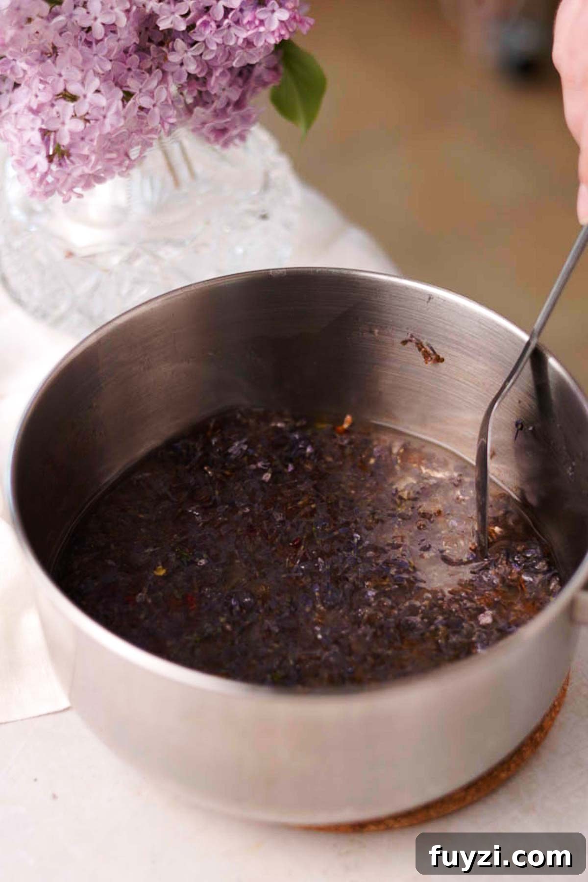 Lilac Lemonade Recipe: How to Make a Floral Citrus Drink 7 stirring cooked lilac syrup in a saucepan with a spoon