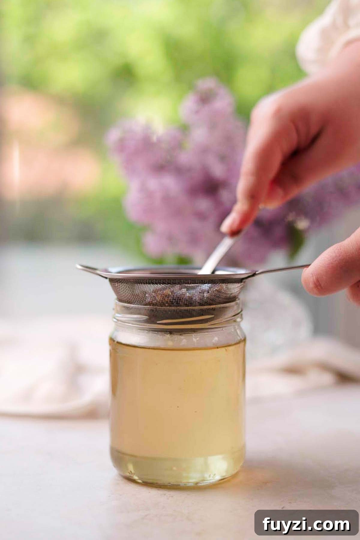 Lilac Lemonade Recipe: How to Make a Floral Citrus Drink 8 straining lilac syrup through a metal sieve into a glass jar