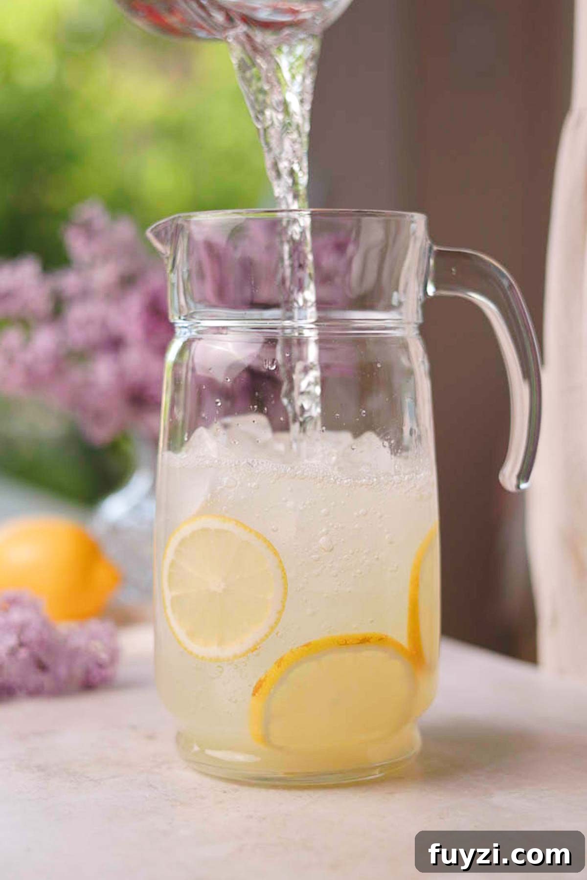 Lilac Lemonade Recipe: How to Make a Floral Citrus Drink 10 pouring water into a glass pitcher with lemon juice and ice