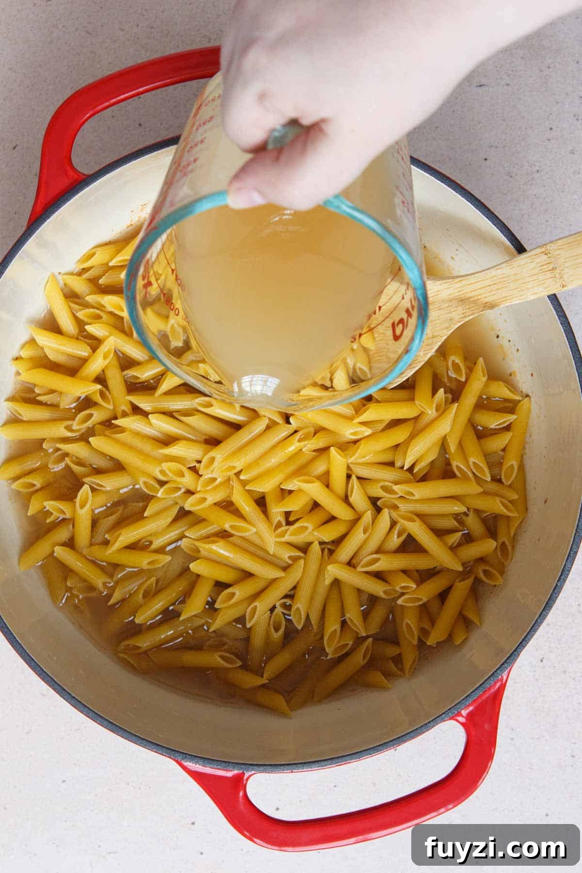 Pouring broth into the pot over the penne