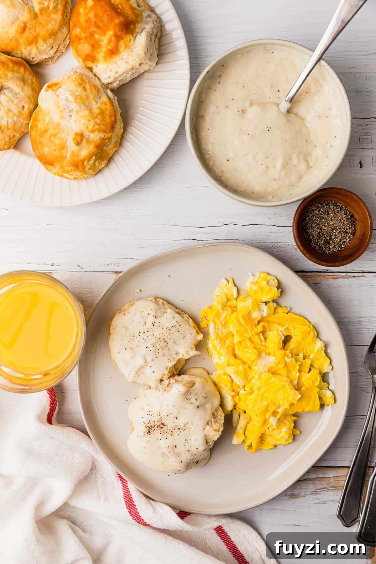 a table of biscuits covered in a white gravy with a side of eggs