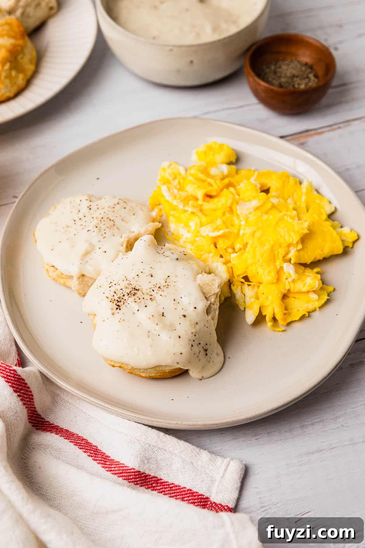 a plate with a breakfast meal of biscuits, gravy, and scrambled eggs