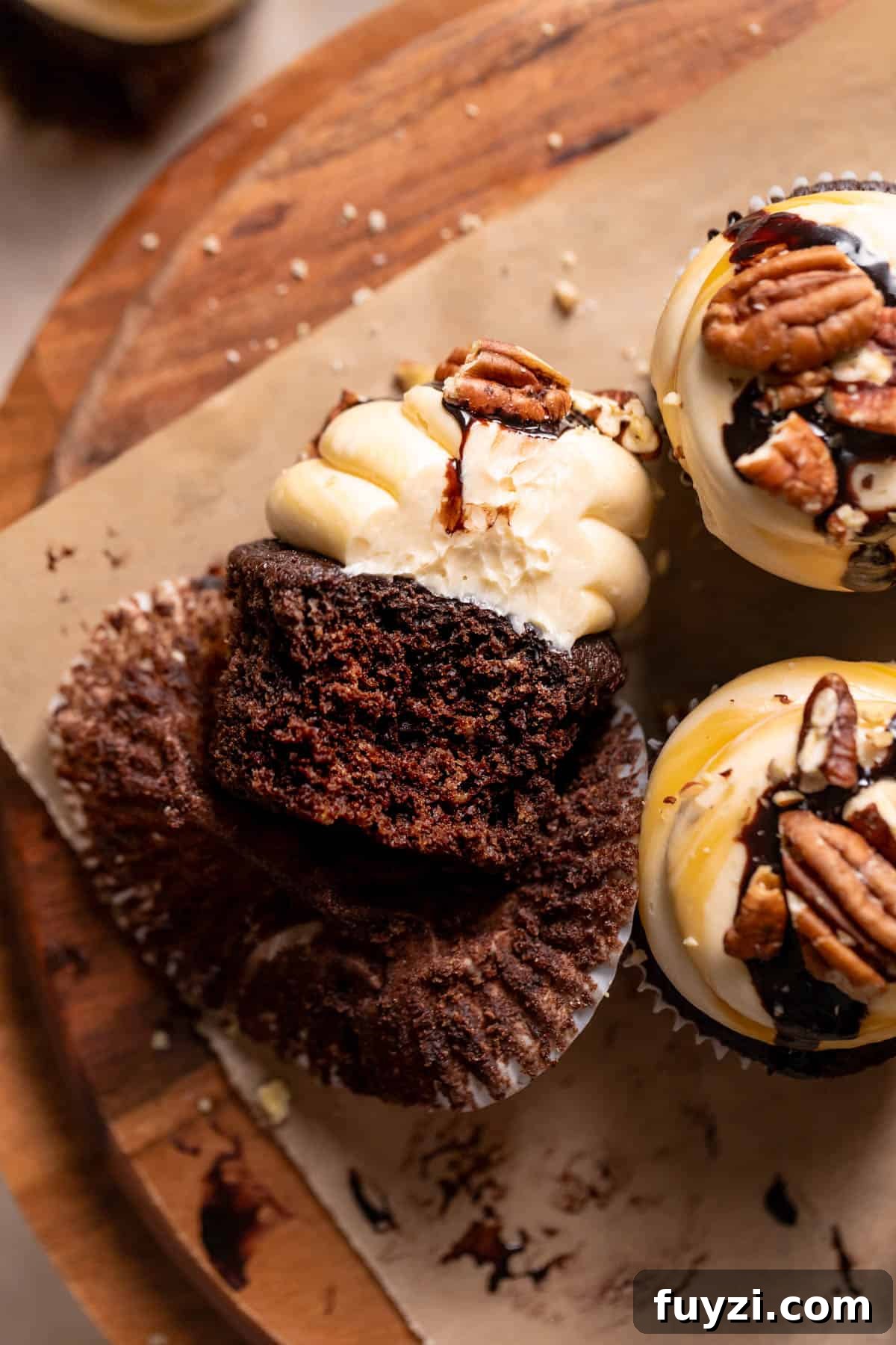 Chocolate Turtle Cupcakes Recipe with Caramel and Pecans 6 A chocolate cupcake with a bite taken out of it on a wooden serving board.