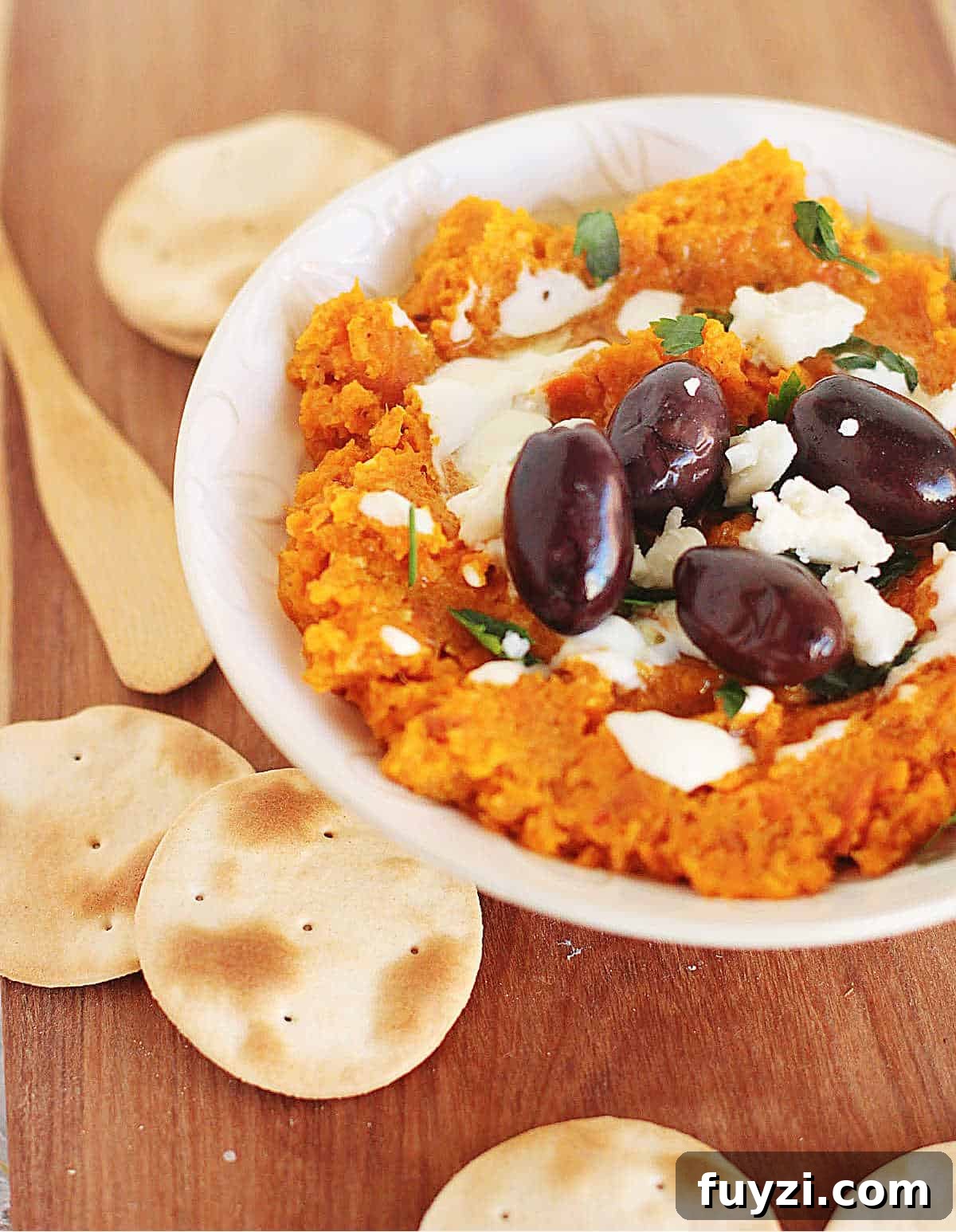 Bowl of carrot dip, black olives, goat cheese and crackers.