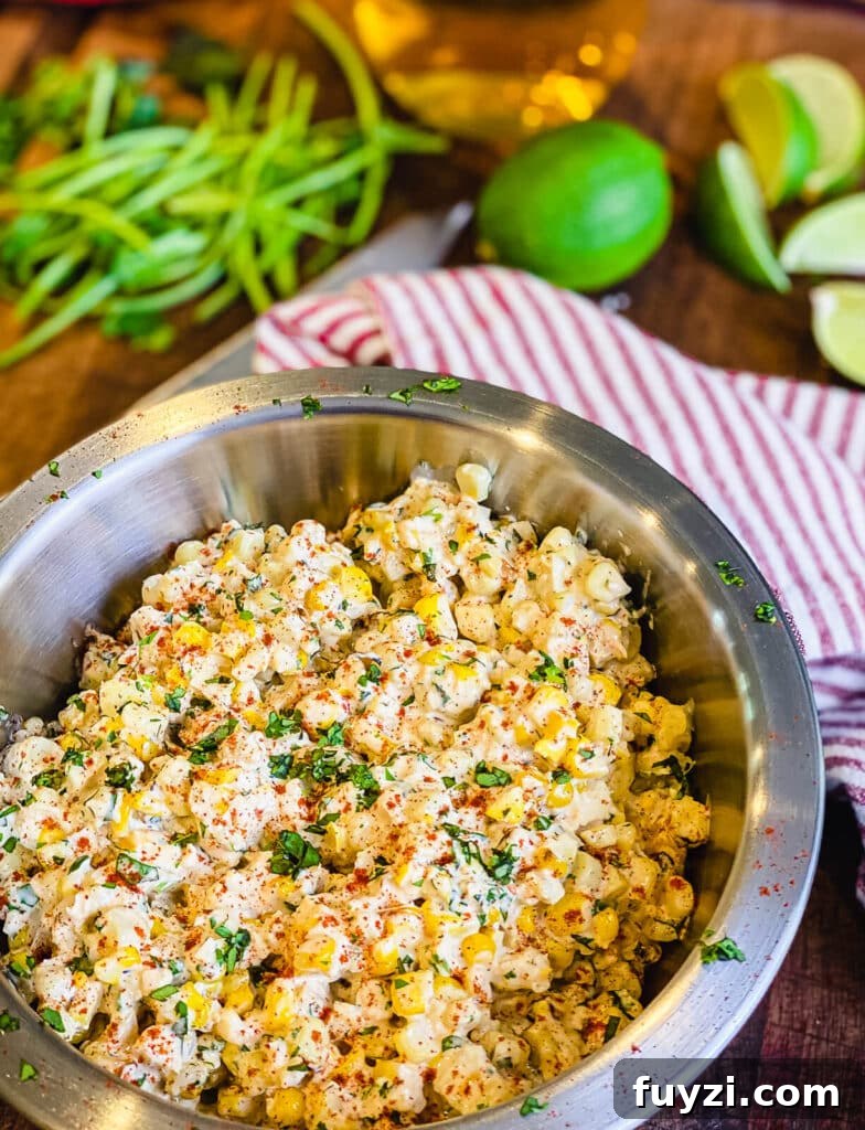 esquites mixed in a large bowl sitting on a cutting board with limes and a knife