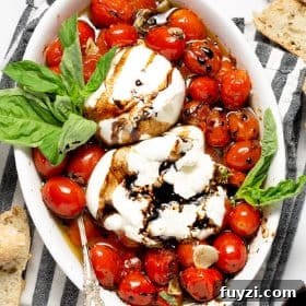 Overhead shot of a white platter filled with roasted tomatoes and burrata garnished with basil
