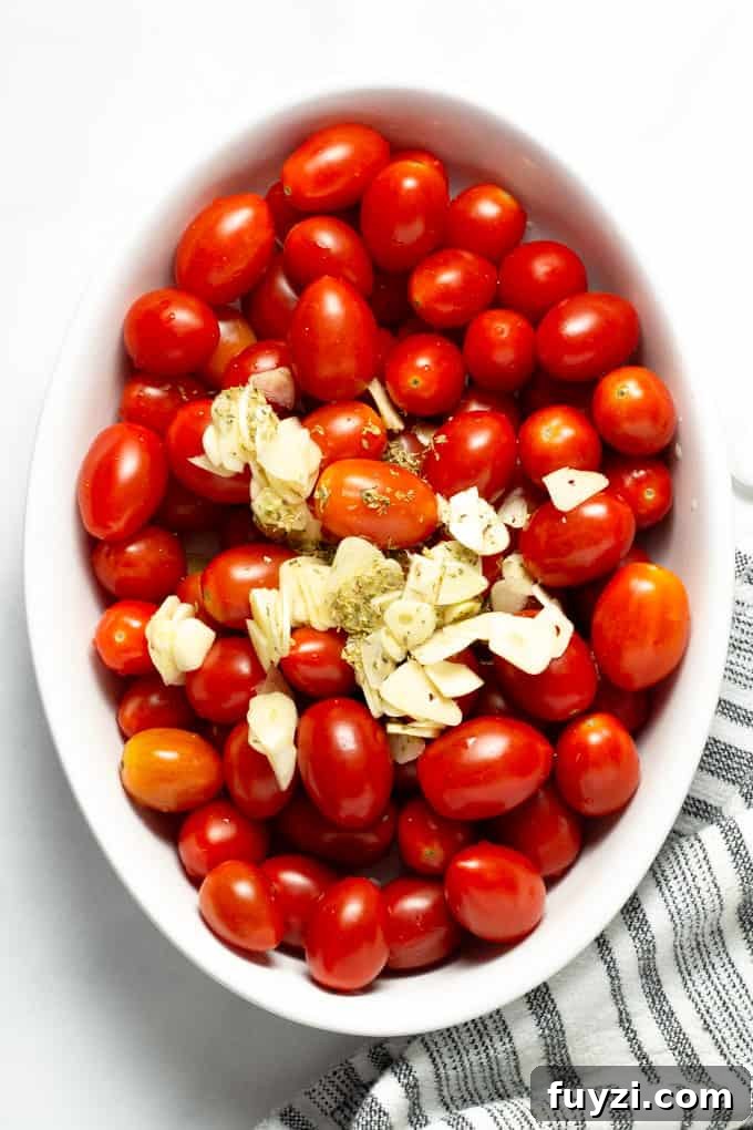 Overhead shot of grape tomatoes topped with sliced garlic, dried oregano and olive oil