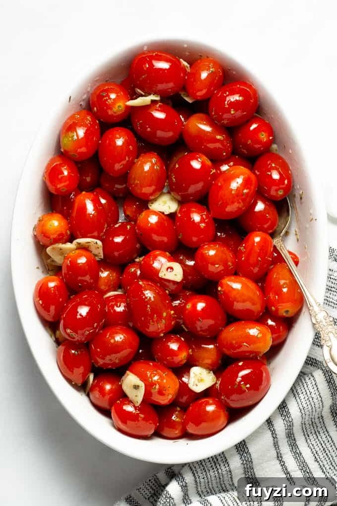 Overhead shot of a white oval baking dish filled with grape tomatoes tossed with olive oil, garlic and oregano