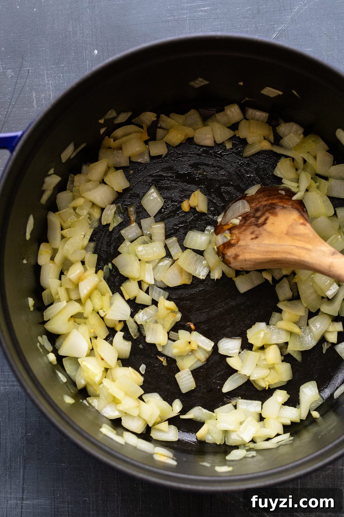 Curried Butternut Squash Soup Recipe 4 A wooden spoon sautéing onions in a black cast iron pot.
