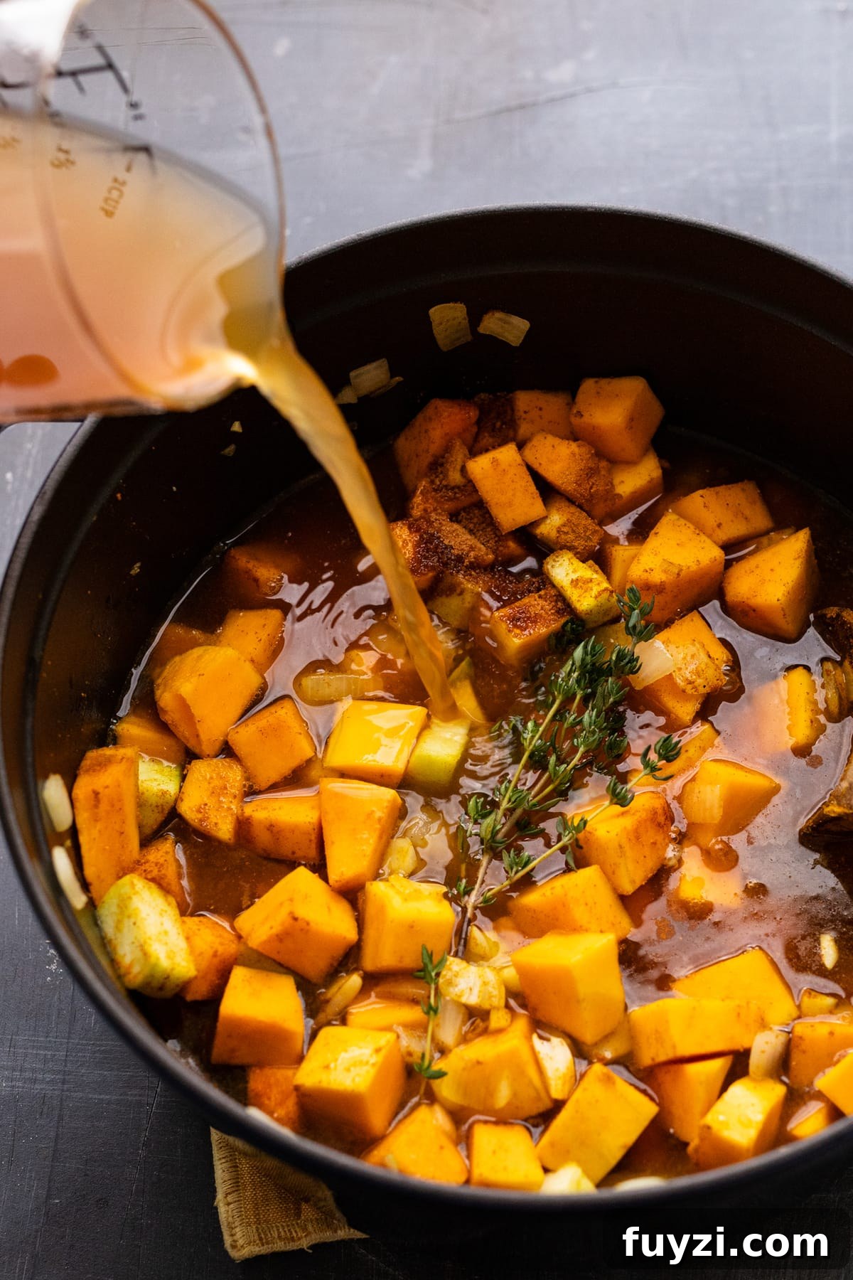 Curried Butternut Squash Soup Recipe 6 Broth being pouring into a black cast iron pot with cubed butternut squash.