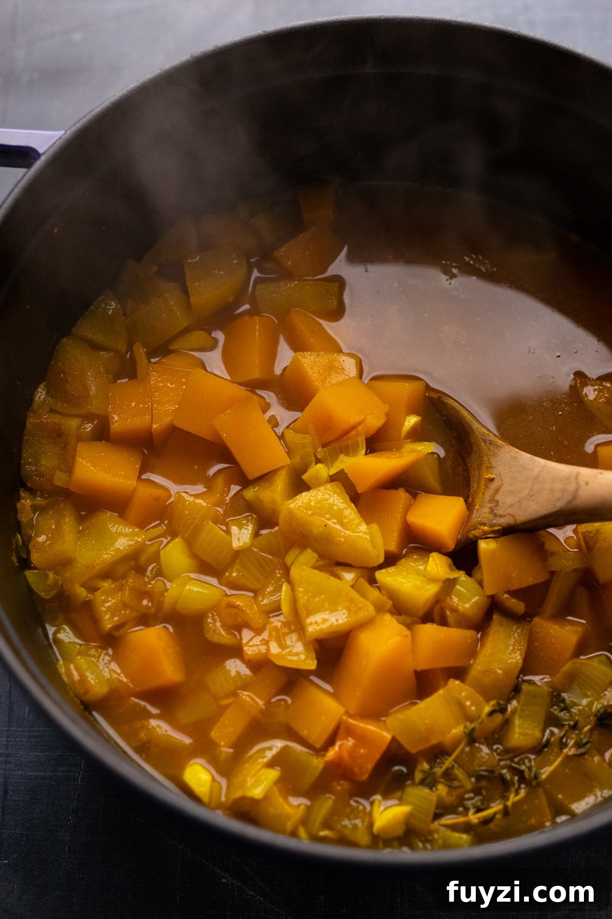 Curried Butternut Squash Soup Recipe 8 A wooden spoon stirring cooked squash in broth.