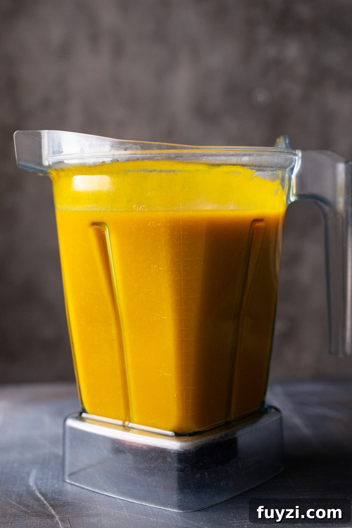 Curried Butternut Squash Soup Recipe 9 Creamy butternut squash soup in a blender container sitting on a gray background.