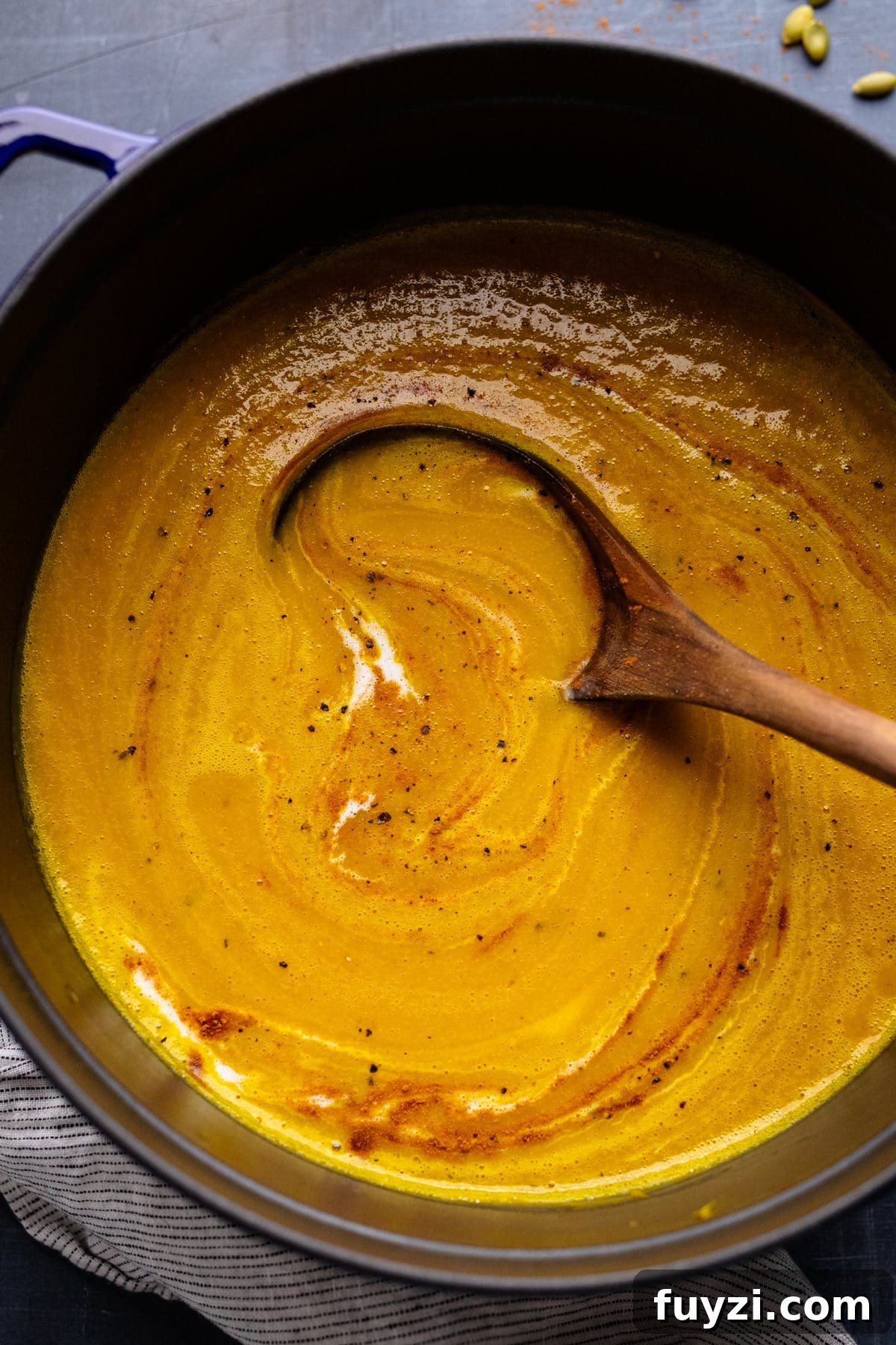 Curried Butternut Squash Soup Recipe 10 A cast iron pot with creamy curried butternut squash soup in it with a wooden spoon.