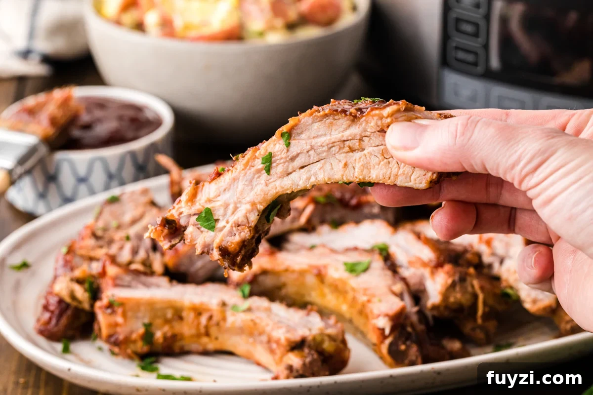 A hand holding up one of the slow cooker baby back ribs.