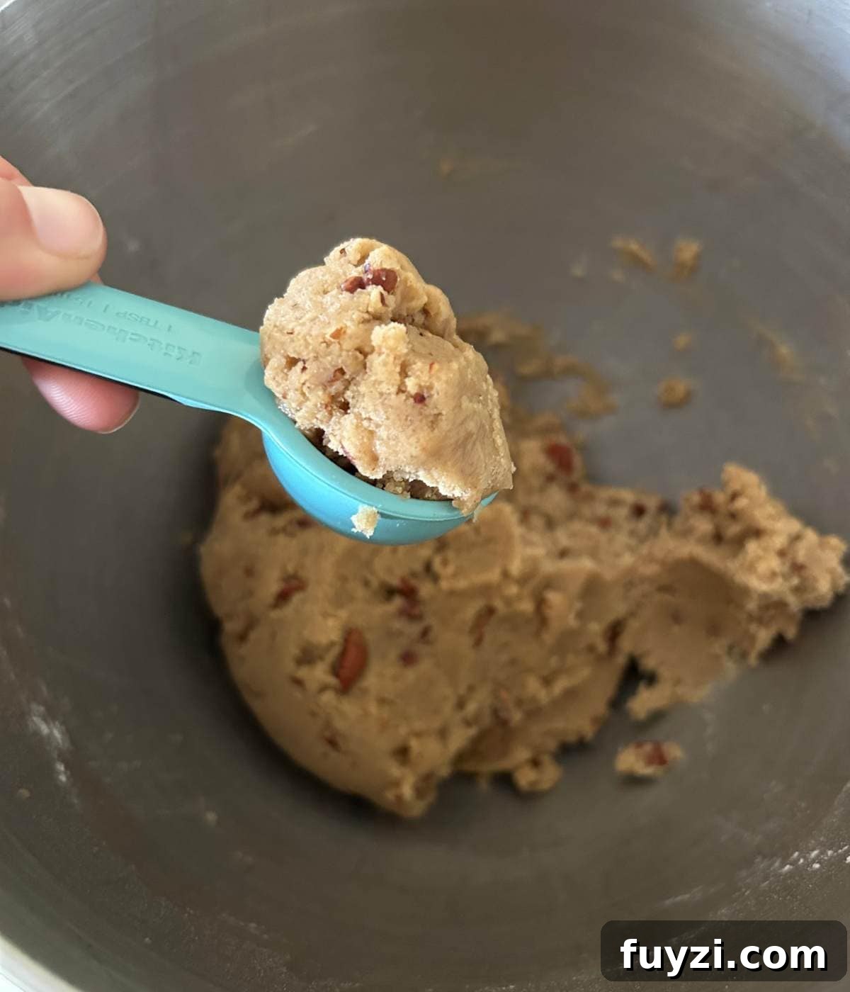 Hand holding tablespoon full of cookie dough.