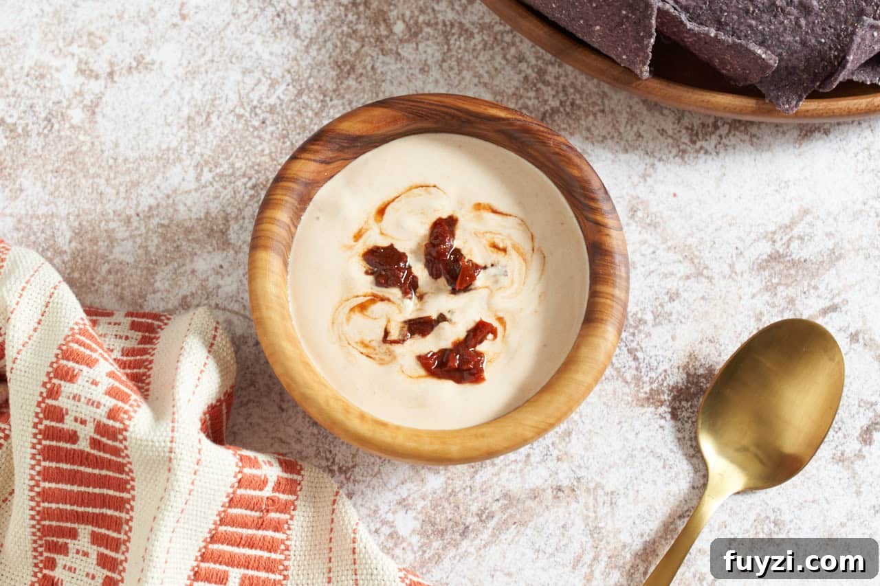 Chipotle crema topped with chopped chipotles in a wooden bowl, a gold spoon is on the right, blue corn chips are in the upper right.