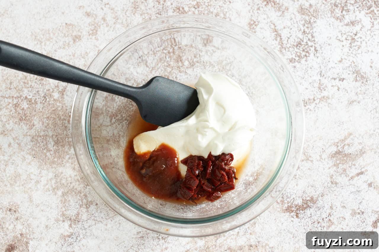 A bowl of sour cream and chipotle chilis in adobo with a black spatula in it.