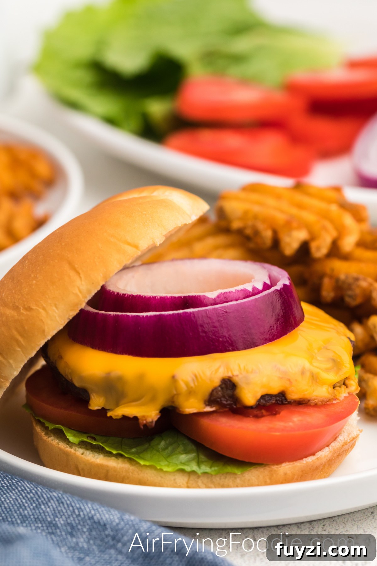 How to Cook a Frozen Burger in an Air Fryer 2 Air fried frozen burger topped with cheese, onions, tomatoes, and lettuce, and served with a side of waffle fries.