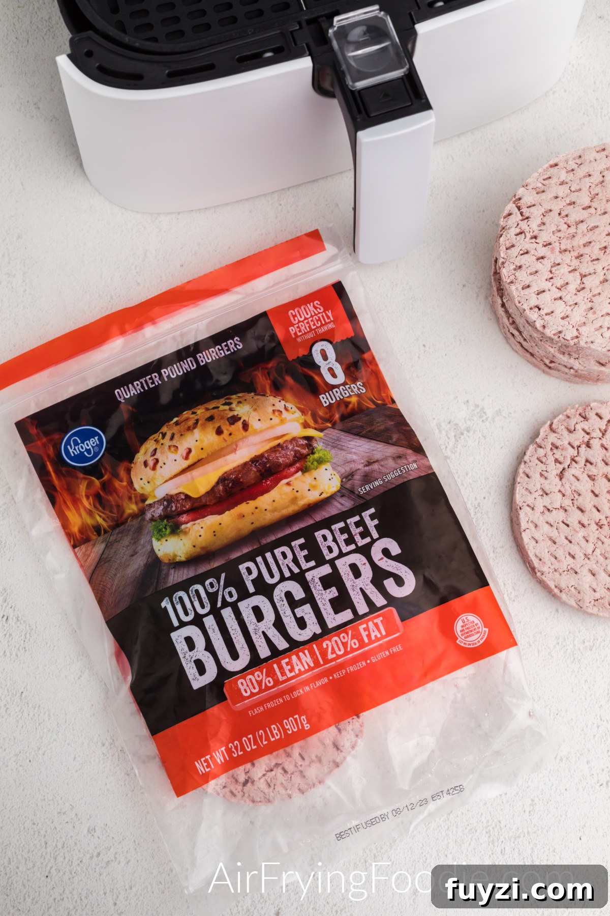 How to Cook a Frozen Burger in an Air Fryer 3 Frozen burger patties and air fryer basket on a table top.