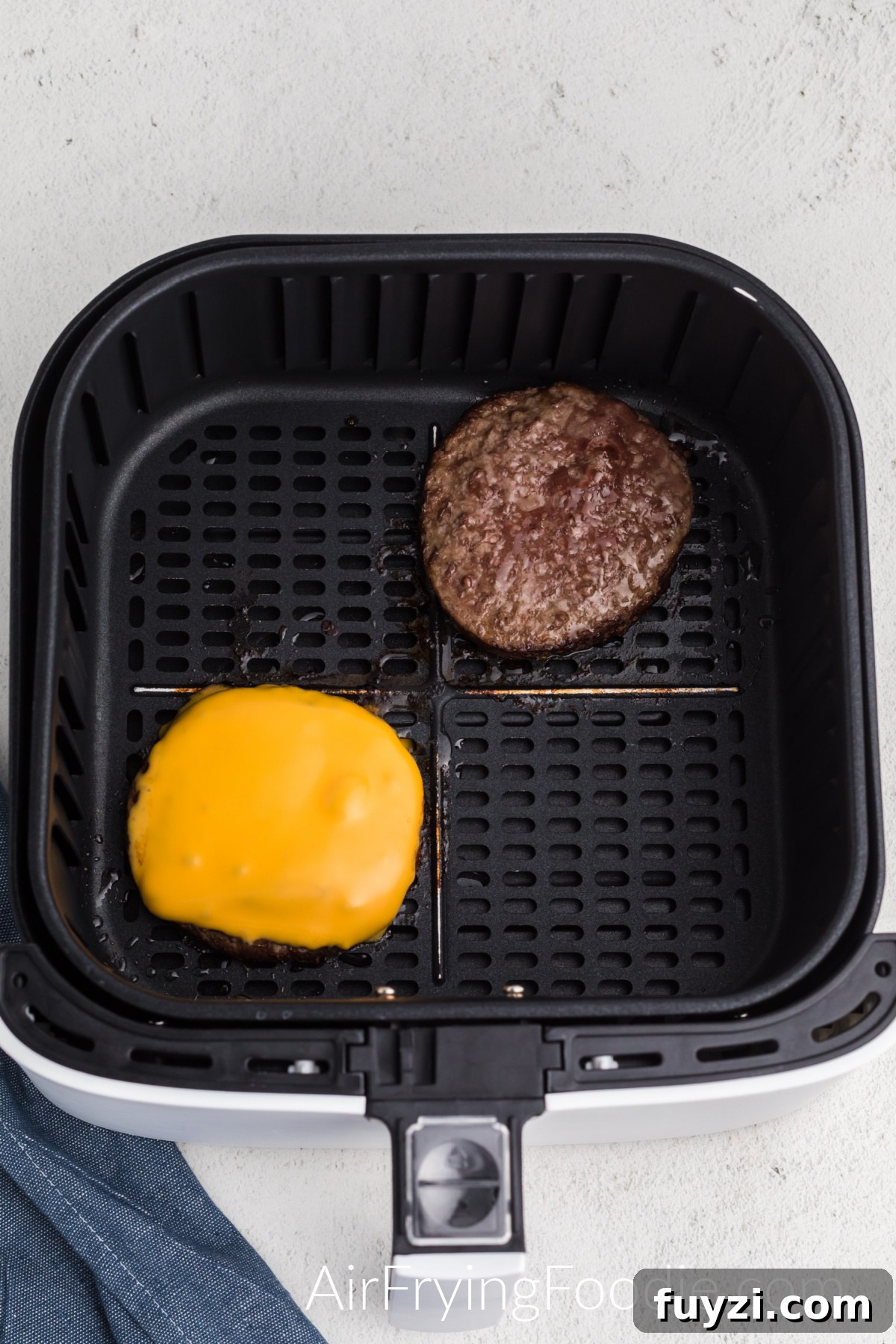 How to Cook a Frozen Burger in an Air Fryer 5 Cooked frozen burger in air fryer basket, one topped with sliced cheese.