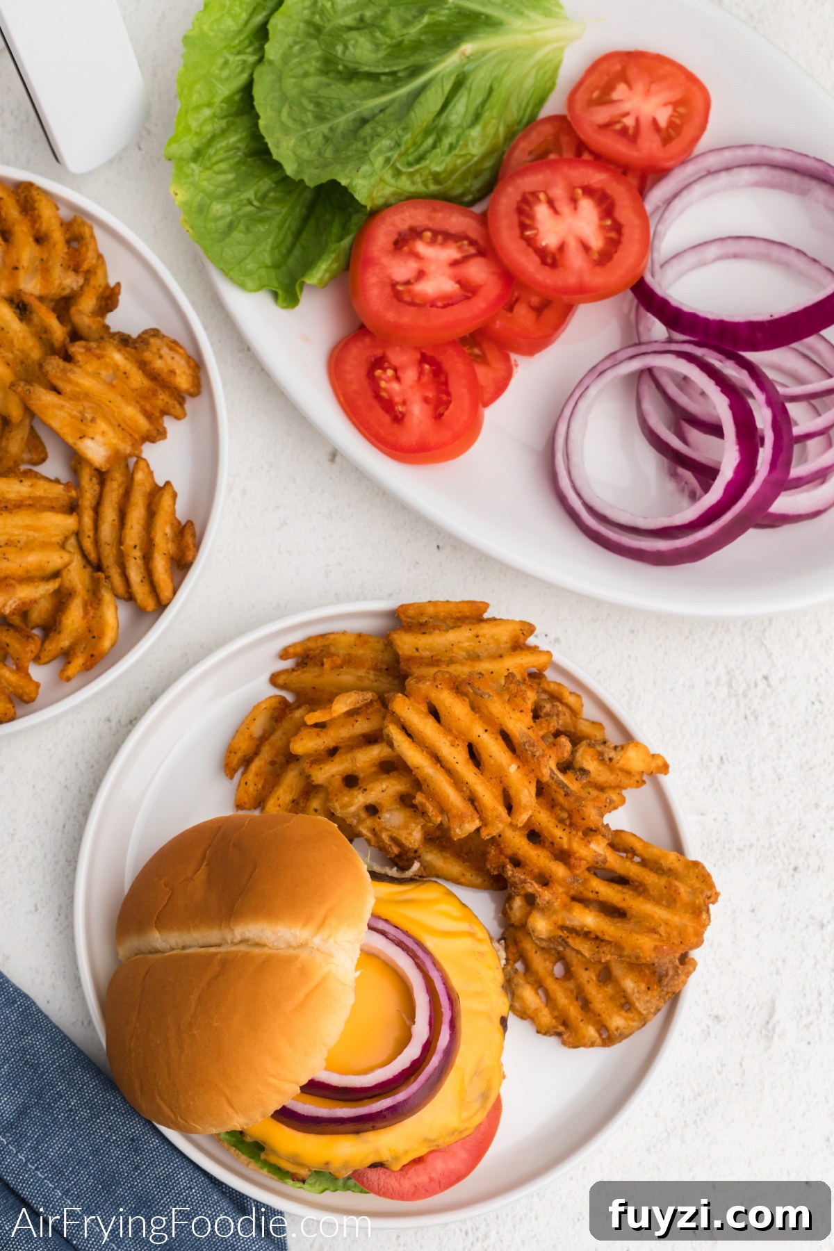 How to Cook a Frozen Burger in an Air Fryer 6 Air fried burger with cheese and topped with onion on a plate with waffle fries.