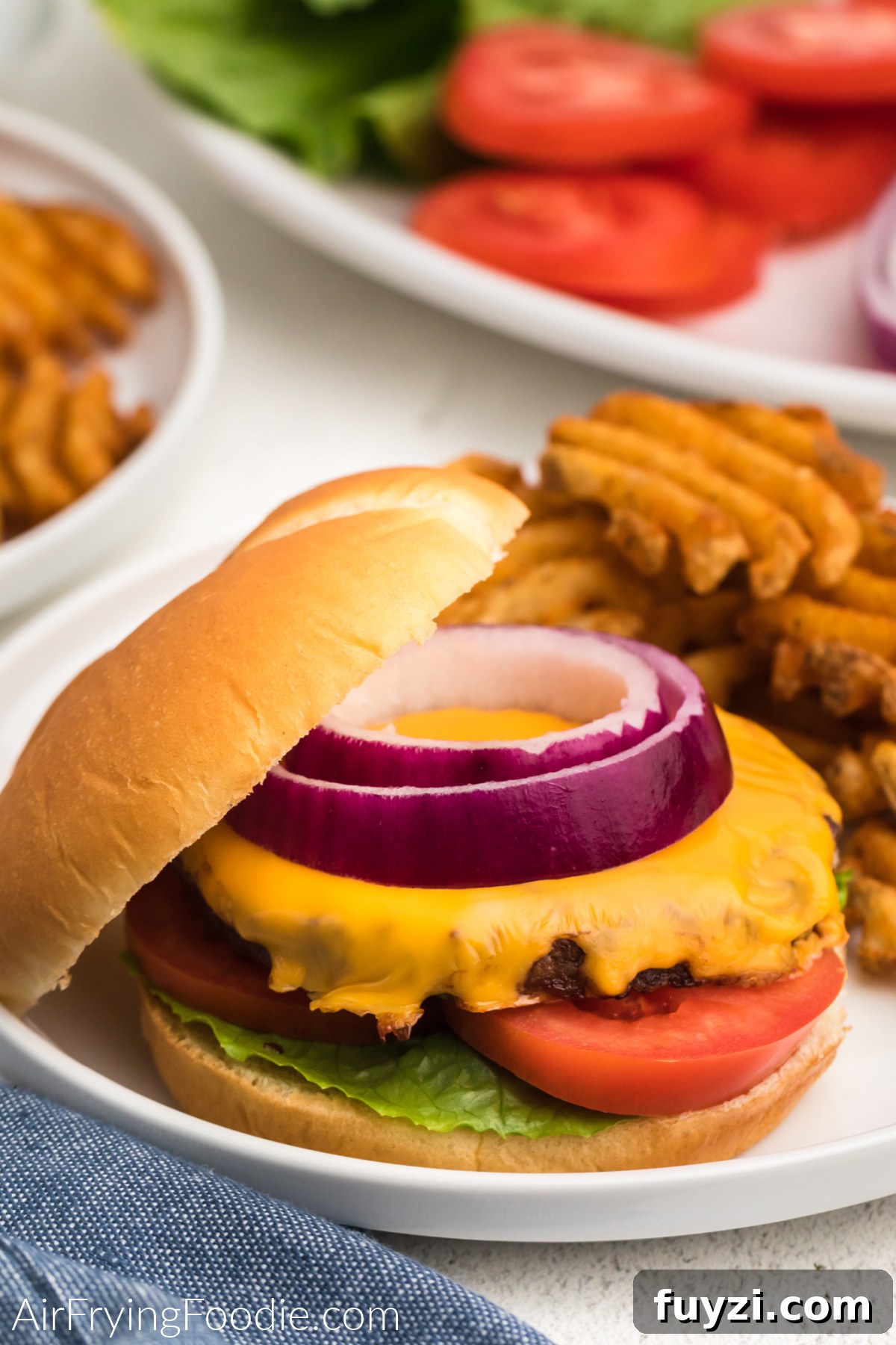 How to Cook a Frozen Burger in an Air Fryer 8 Air fried frozen burger topped with cheese, onion, tomato, and lettuce, and served on a plate with waffle fries.