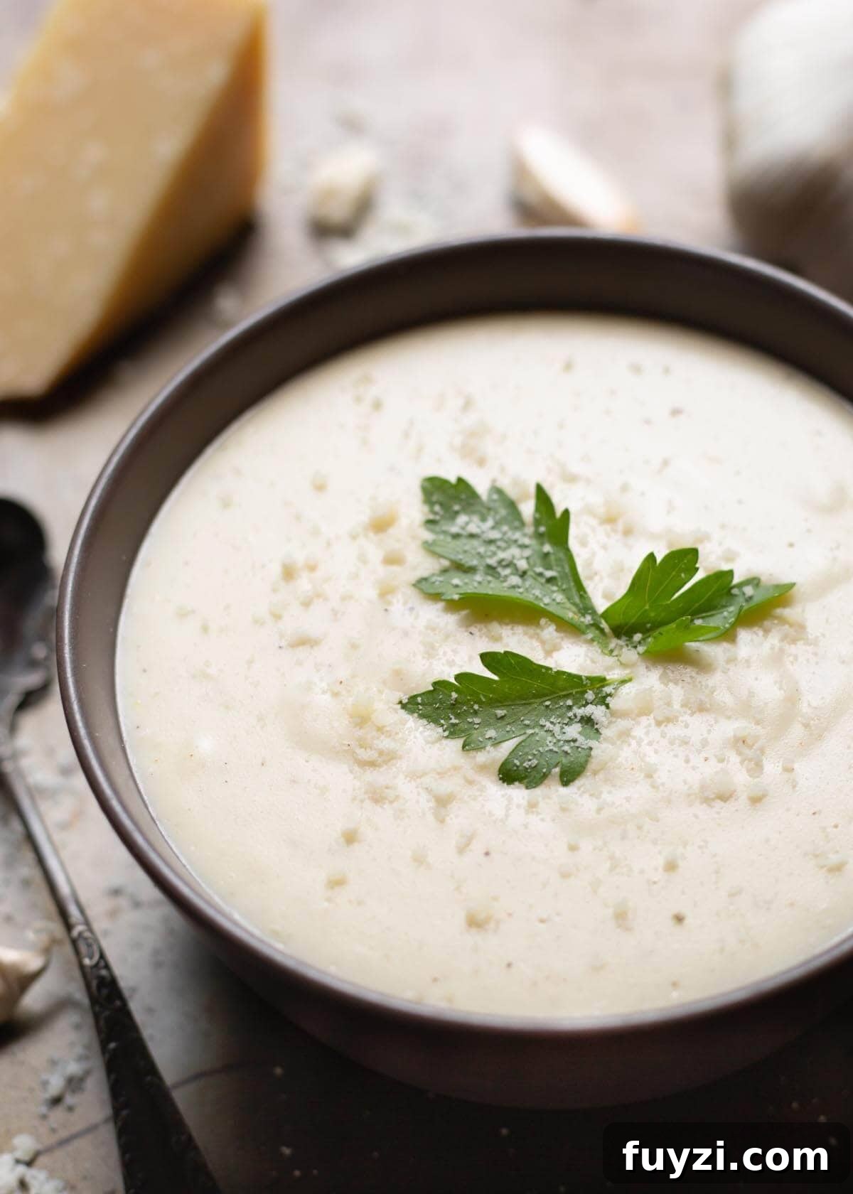 Creamy Garlic Parmesan Sauce Recipe 2 Garlic Parmesan Cream Sauce in a black bowl on a wooden board garnished with parsley