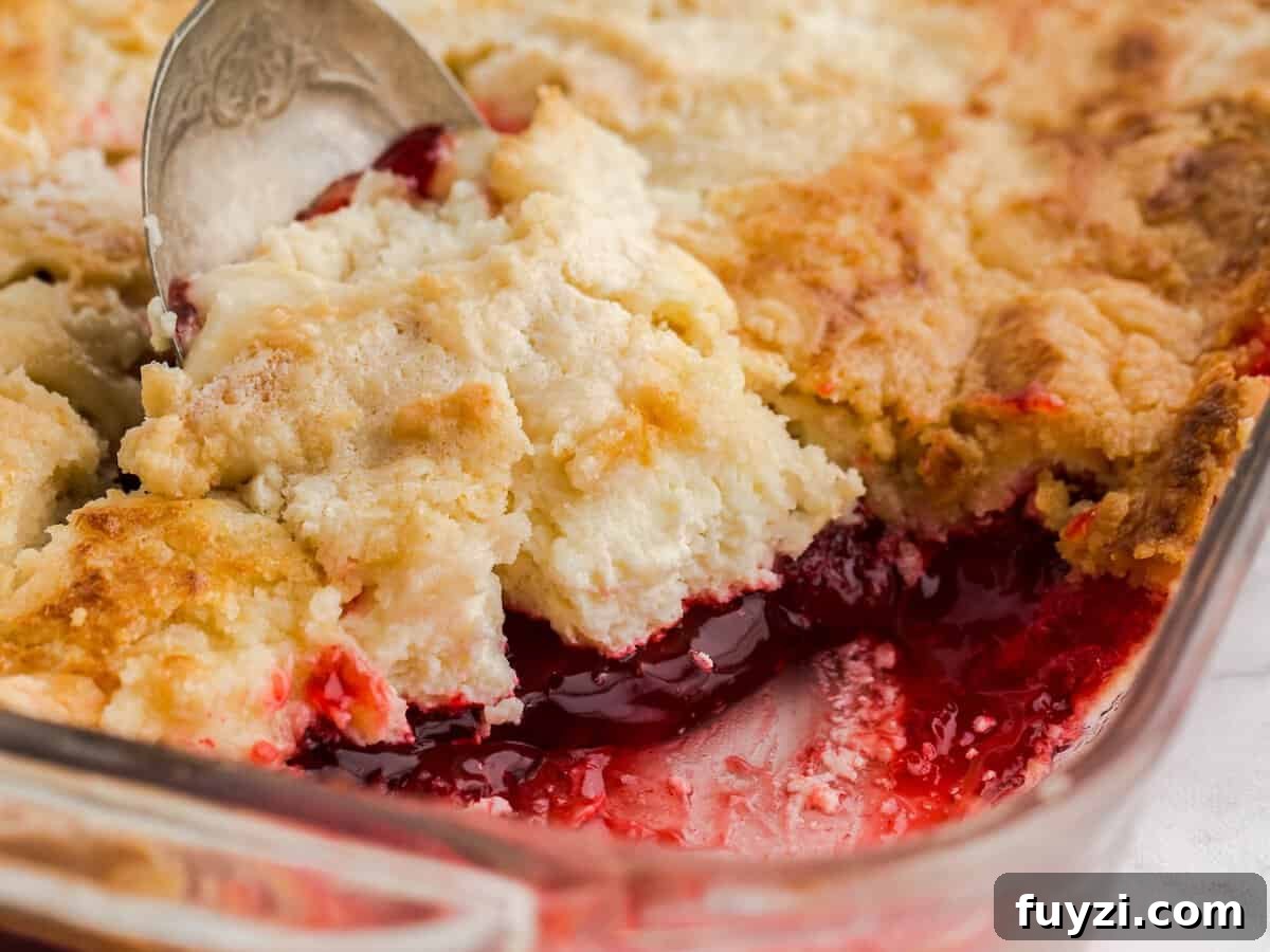 A close-up of a strawberry dump cake in a glass baking dish, with a spoon lifting a portion to reveal the gooey red fruit filling beneath a golden, crumbly crust—an irresistible strawberry dump cake recipe come to life.