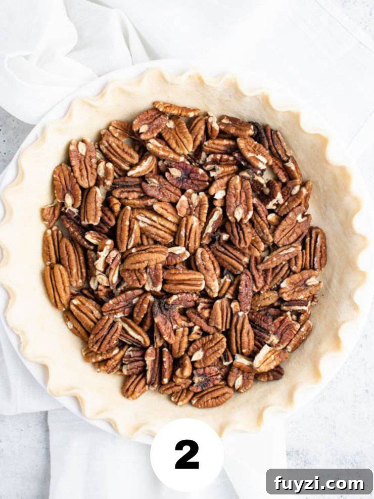 How to Make Bourbon Pecan Pie Without Corn Syrup 4 pie crust in a white pie pan filled with halved pecans.