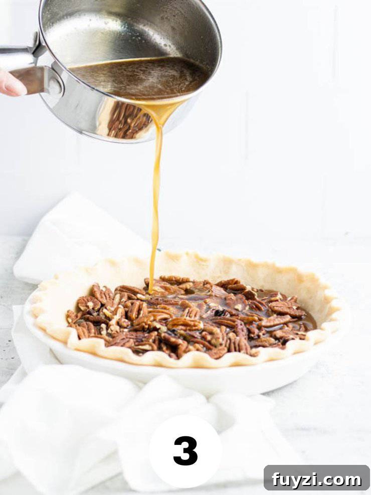 How to Make Bourbon Pecan Pie Without Corn Syrup 5 hot syrup mixture being poured from a small silver saucepan into a pie crust with pecans.