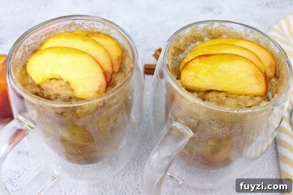 two peach mug cakes in see through mugs with fresh peach slices on top