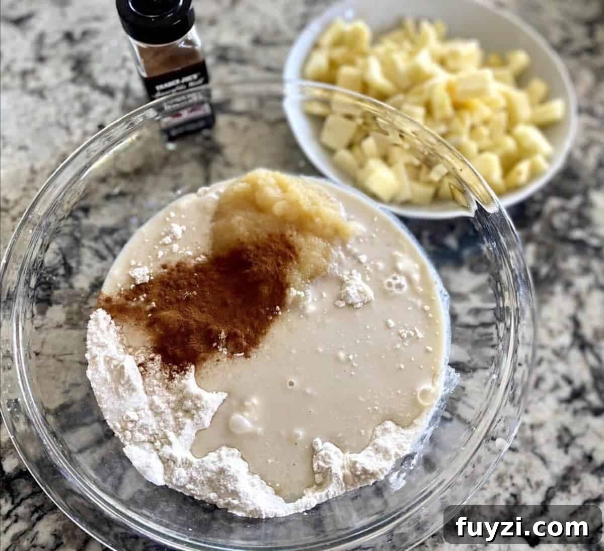 Apple cinnamon bread recipe ingredients in a bowl with peeled, chopped apples in a bowl with cinnamon on the counter.  
