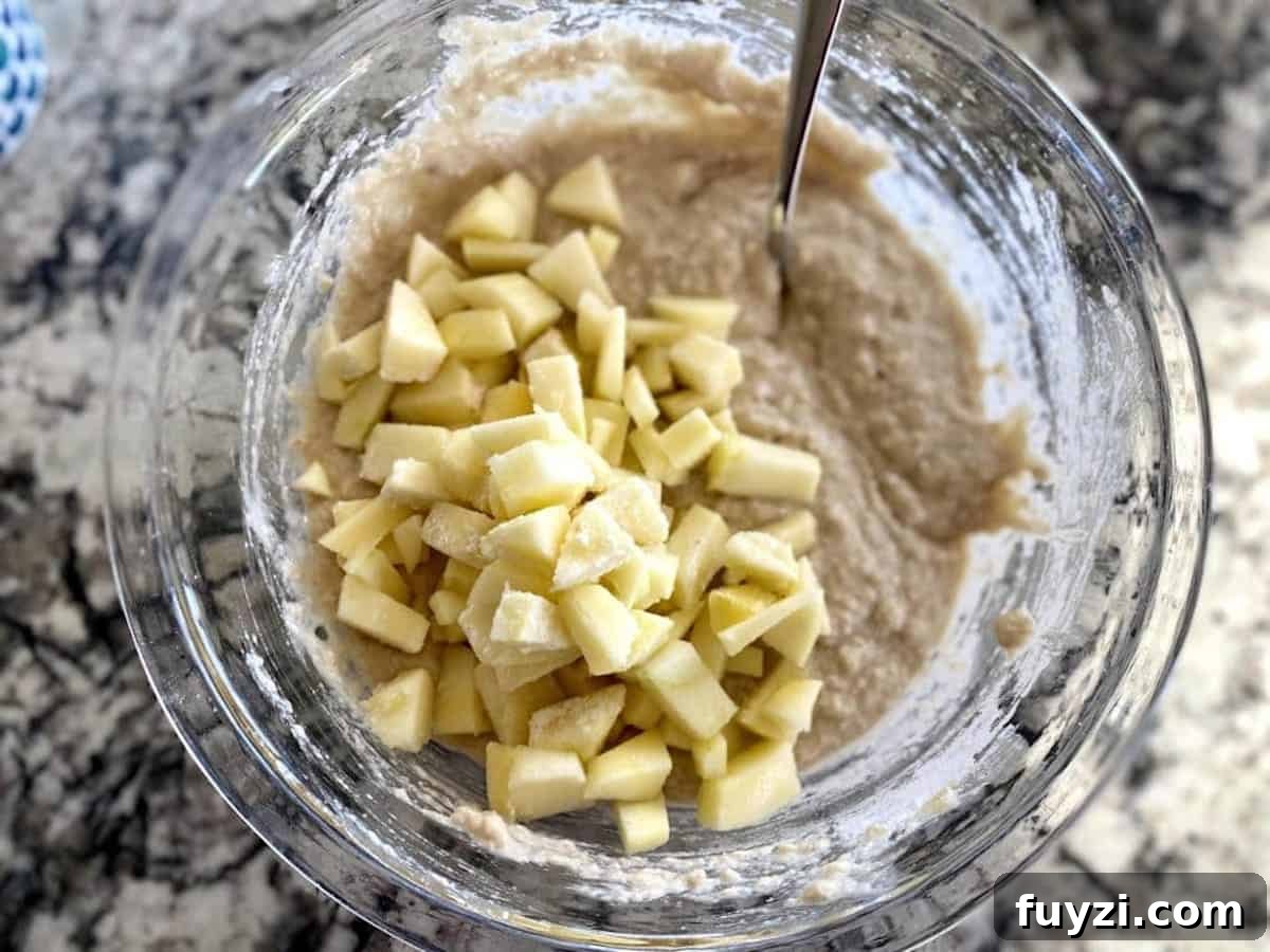 Adding cut, peeled apples to the bread batter in a bowl on the counter
