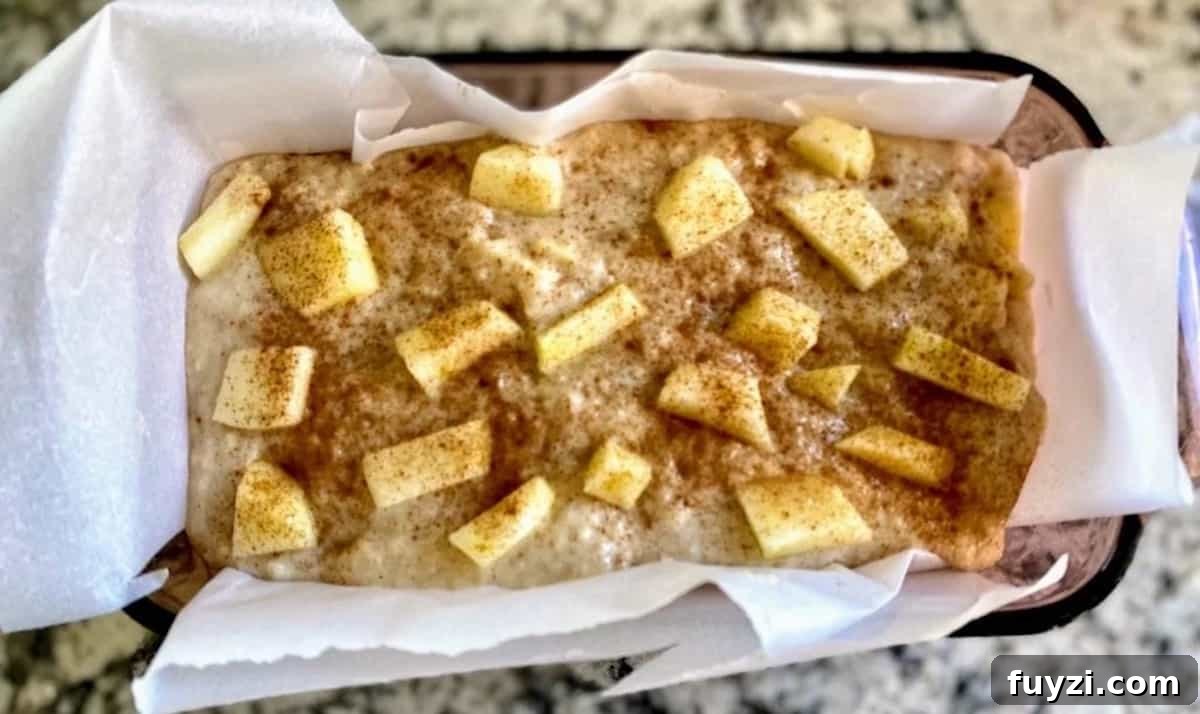 Apple cinnamon batter in a bread pan lined with parchment paper topped with cinnamon apples. 