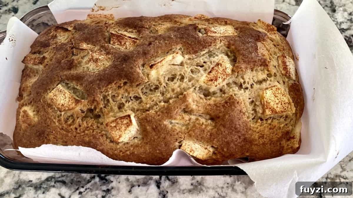 Baked apple cinnamon bread in a pan lined with parchment paper on the counter. 