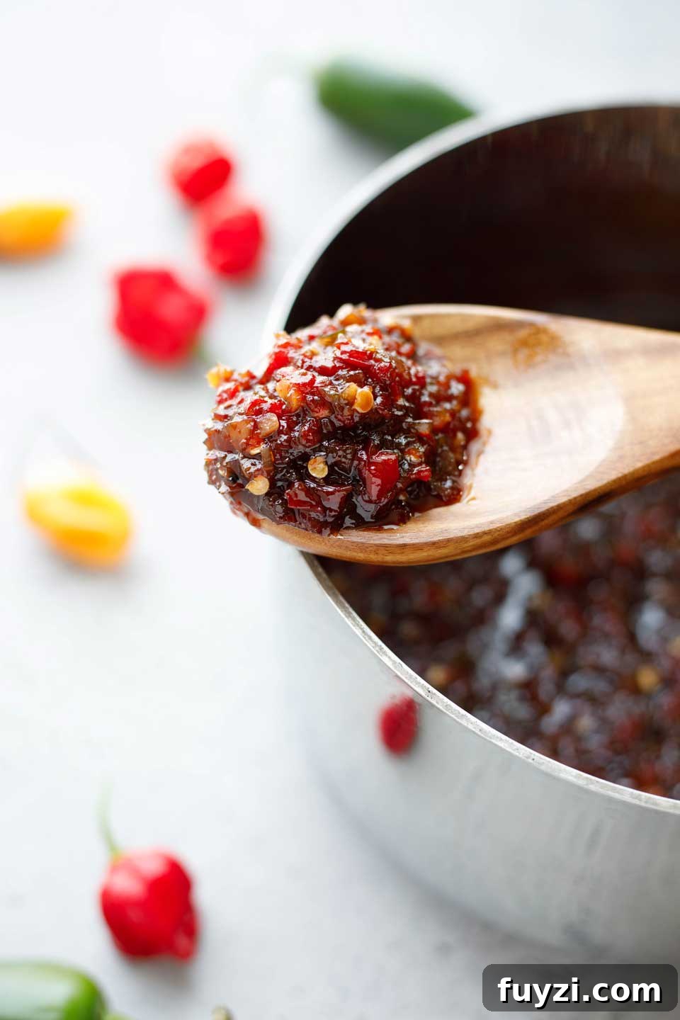 Closeup of wooden spoonful of cooked pepper relish, laid across the cooking pot.