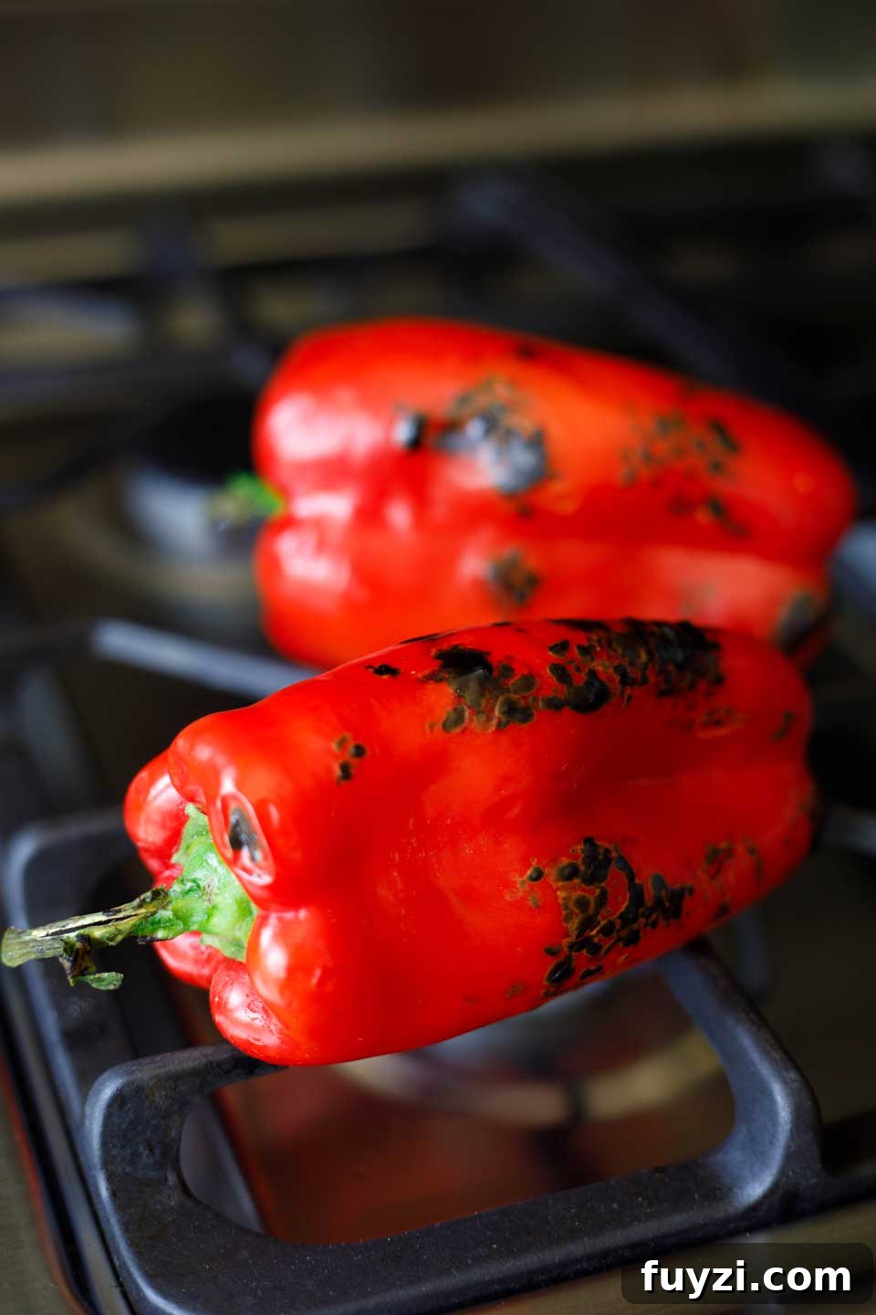 Two red peppers roasting on a gas stove.