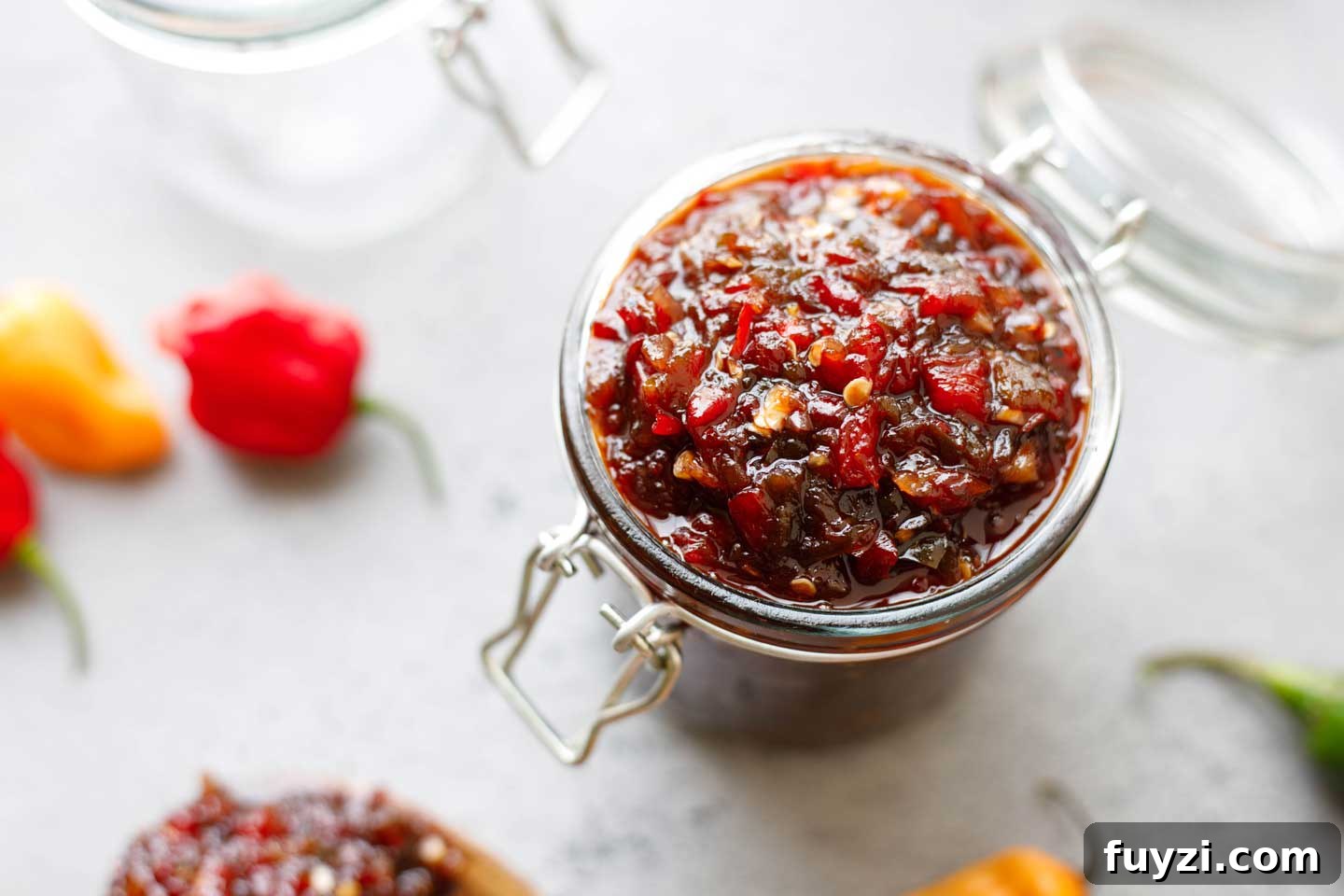 Overhead of jelly jar filled with pepper relish, with a few hot peppers scattered nearby.