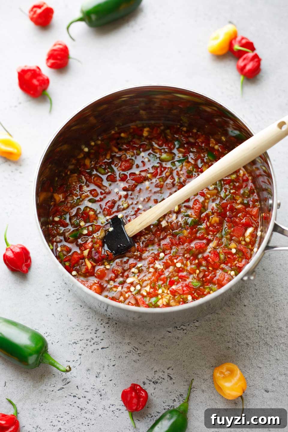 Large silver pot full of ingredients being stirred, with raw hot peppers scattered in background.