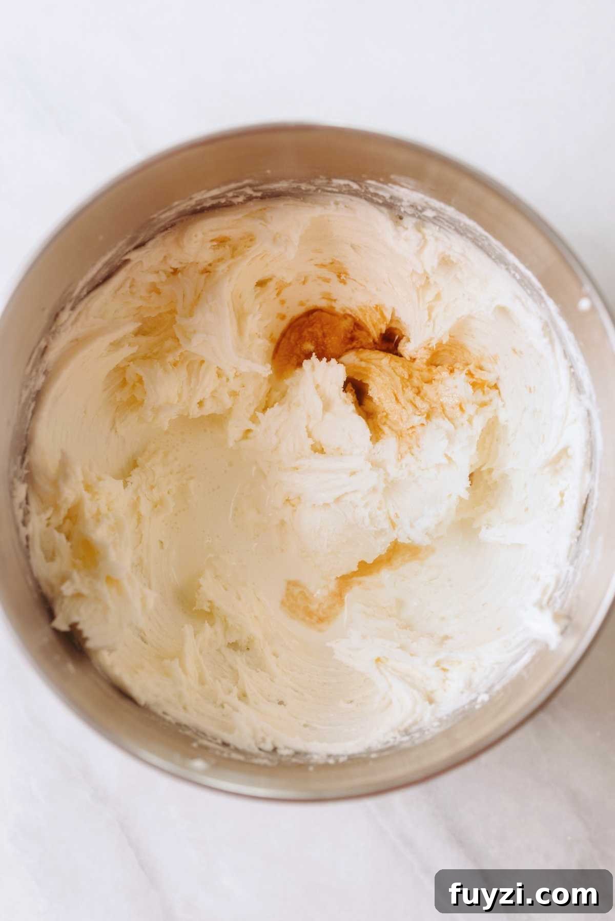 Powdered sugar, vanilla, and heavy cream added to the metal mixing bowl with creamed butter.