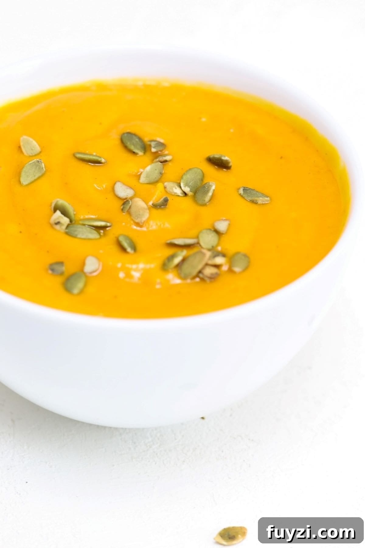 Carrot Butternut Squash Soup in a white bowl and topped with pumpkin seeds.